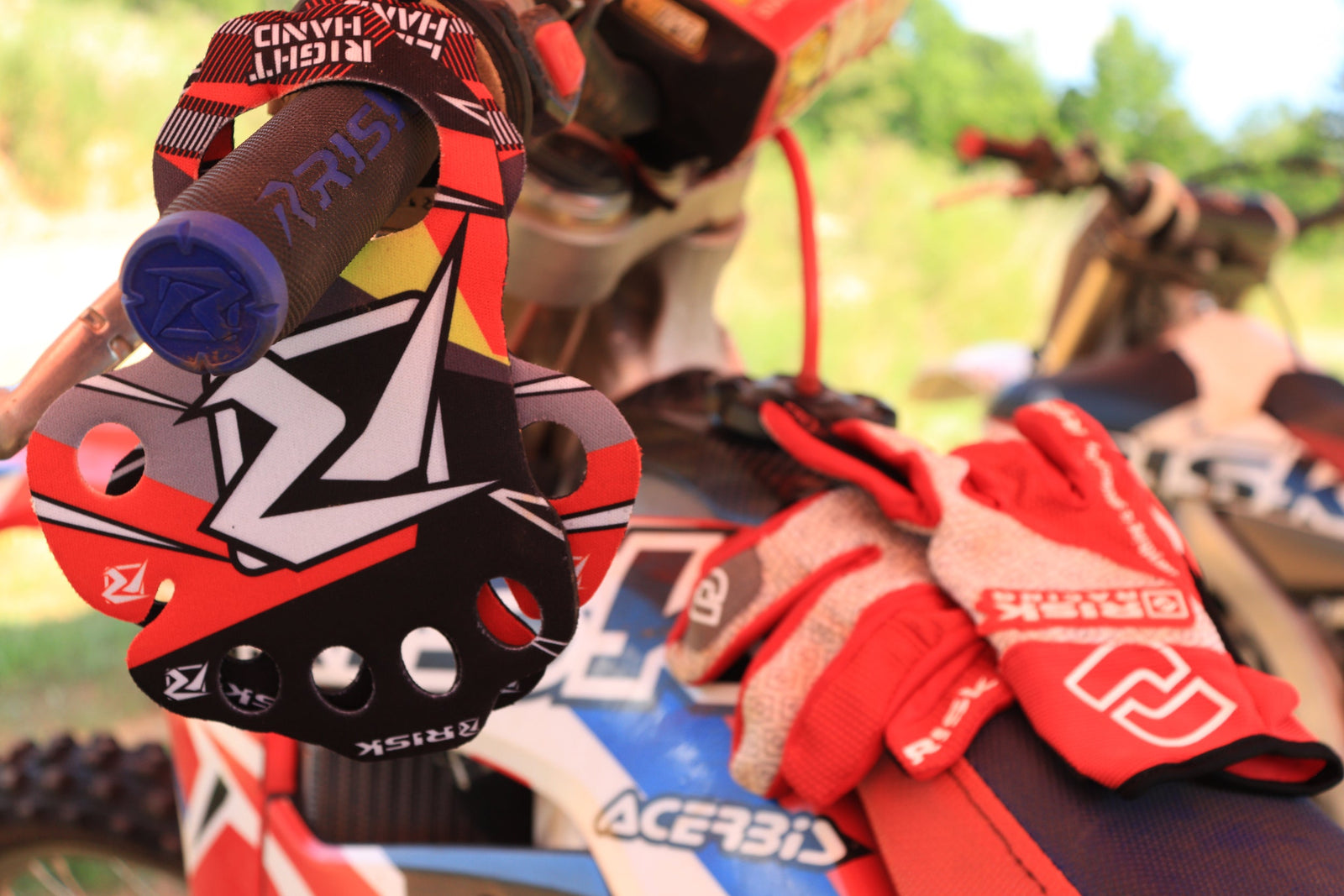 palm protectors hanging on a set of dirt bike handlebars equipped with Fusion 2.0 Grips by Risk Racing